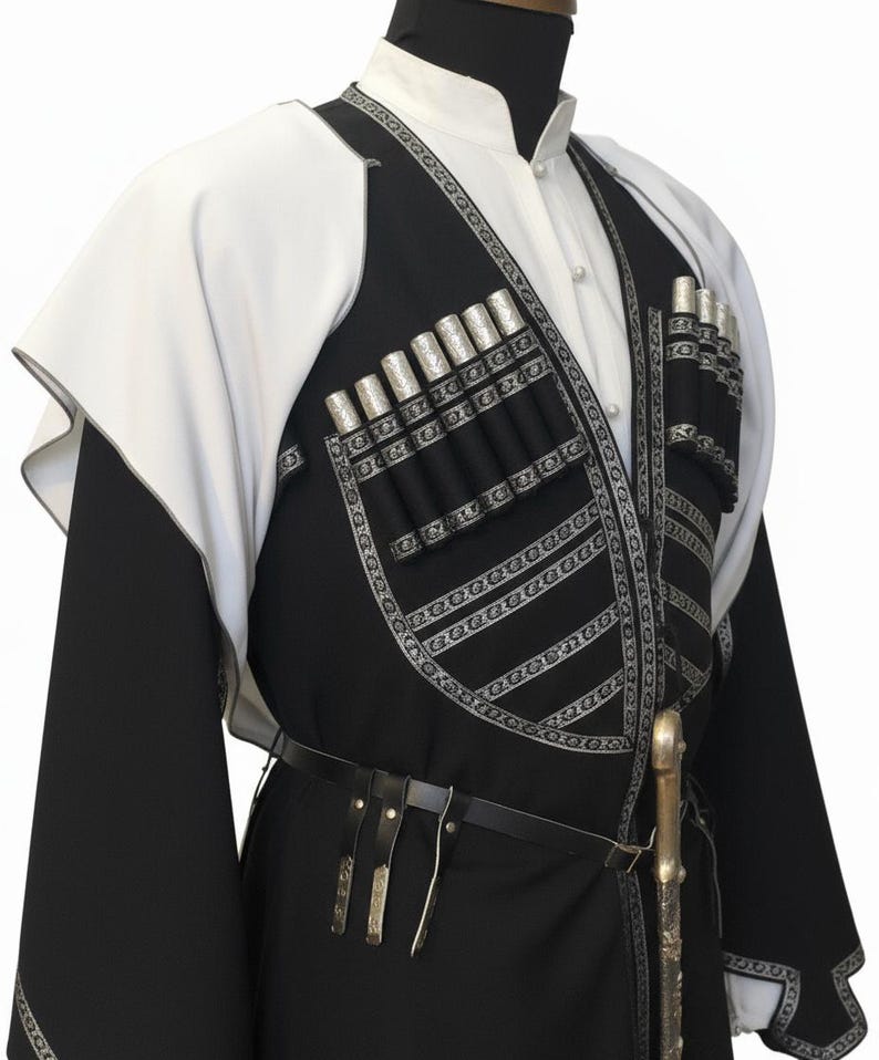 May include: A traditional black and white outfit with silver detailing. The outfit includes a high-collared white shirt, a black vest with silver embellishments, and a black belt. The vest has multiple silver cylindrical decorations. A decorative sword is attached to the belt.