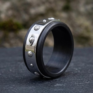 May include: A black and silver ring with a planetary design. The ring has a dark band with a silver outer band decorated with small planet-shaped embellishments. The ring is displayed on a dark surface.
