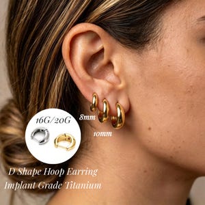 May include: Three gold-colored D-shaped hoop earrings of varying sizes are worn in the earlobe. The text 16G/20G, 8mm, and 10mm is visible. An inset shows a silver and a gold hoop earring. The text D Shape Hoop Earring Implant Grade Titanium is present.