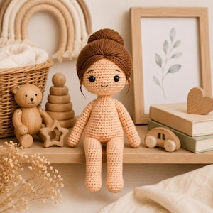 Può includere: Una bambola all'uncinetto fatta a mano con pelle beige chiaro e capelli in filato marrone scuro raccolti in uno chignon alto. La bambola ha occhi neri ricamati e un piccolo sorriso, con un corpo semplice e senza decorazioni in filato seduta.