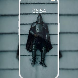 Może przedstawiać: Smartfon z ekranem blokady z tekstem Fallen frost... Exclusively optimized for your lock screen. Shop the Dark Fantasy Collection. Tapeta przedstawia rycerza w srebrnej zbroi leżącego na śniegu, godzina 06:54 wyświetlona na ekranie.