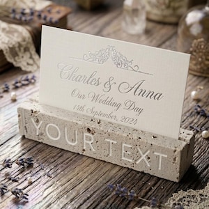 May include: A rectangular concrete block card holder with the words YOUR TEXT embossed on the front. A white rectangular card is inserted into the top slot, featuring the silver printed text Charles & Anna, Our Wedding Day, 14th September, 2024.