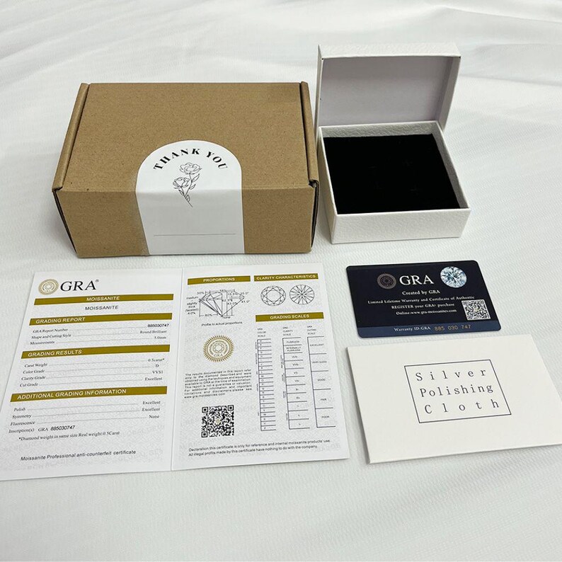 May include: A brown cardboard box with a "Thank You" sticker, a white jewelry box, and a GRA Moissanite grading report. Also included is a card with a diamond graphic and a silver polishing cloth.
