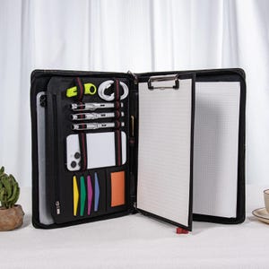 Puede incluir: Portafolio de cuero negro con múltiples compartimentos para organización. Incluye una tableta, un teléfono inteligente, bolígrafos y un bloc de notas con un portapapeles. Cuenta con cierre de cremallera y varios accesorios de colores.