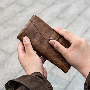 May include: A brown leather wallet with a textured surface. The wallet is rectangular and features a stitched design along the edges. The wallet is held open, showcasing its interior.