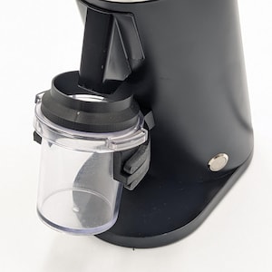 May include: Black electric coffee grinder with a clear plastic container. The grinder has a silver dial with numbers and a textured top. The design is sleek and modern, suitable for home or commercial use.