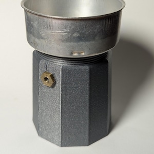 May include: A silver-coloured, octagonal-shaped coffee maker with a removable, silver-coloured top. The coffee maker has a brass-coloured screw on the side.