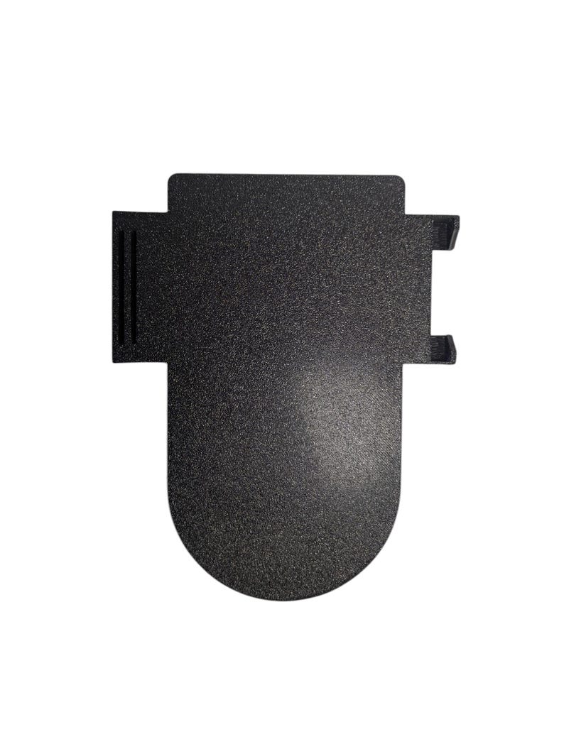 May include: A textured, black metal object with a distinctive shape. It has a rectangular top with two small projections and a rounded base. The surface has a speckled appearance, suggesting a matte finish. The object's design is modern and minimalist.