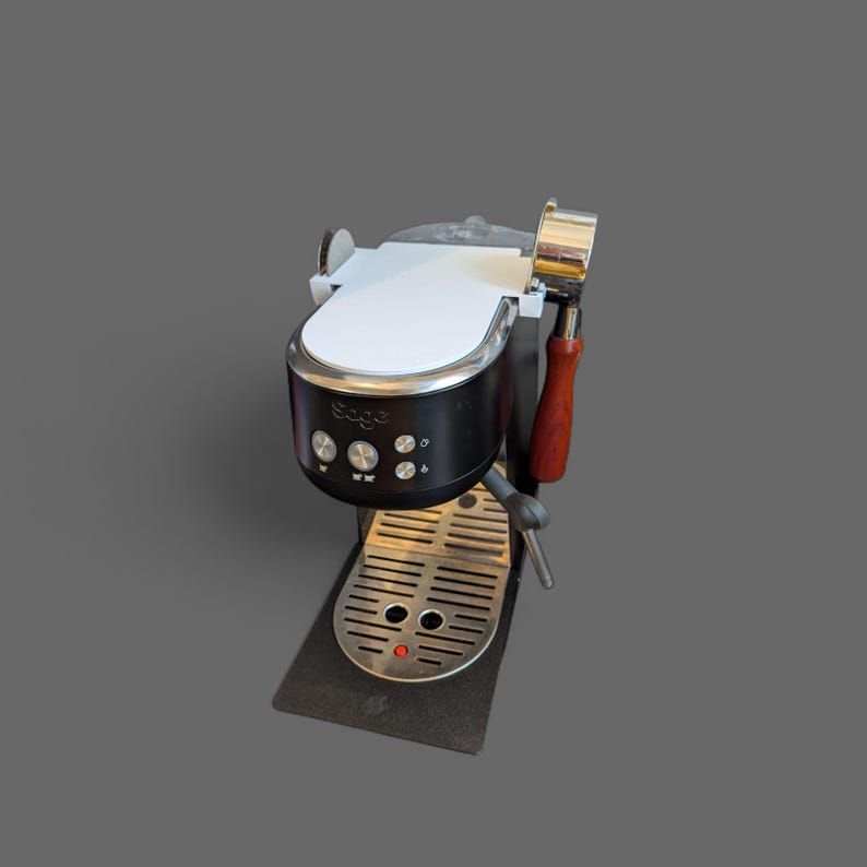 May include: A black and silver espresso machine with a white top and wooden handle. The machine has a stainless steel drip tray and a red light. The brand name "Sage" is visible on the front.