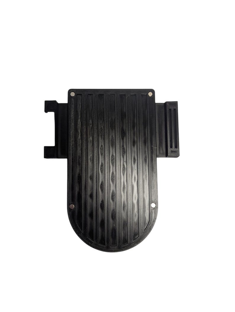 May include: A black plastic automotive component with a ridged surface and a curved base. It features several mounting holes and a rectangular projection on the left. The part is designed for a vehicle.