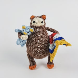 Könnte beinhalten: Ein brauner Häkelbär, der einen blauen Häkelbären und eine bunte Häkeldecke hält.