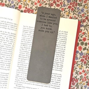 May include: A gray leather bookmark with the quote "A year ago, when I wanted to be around someone like you, I had to, you know, make you up."
