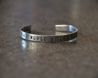 May include: A silver metal bracelet with the words "What Would Stiles Do?" engraved on it.