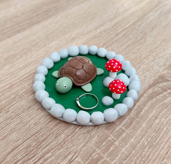 A tiny turtle curled under a mushroom sculpted entirely in polymer clay — the kind of whimsical desk object that makes visitors pick it up and go 'wait, what IS this?'