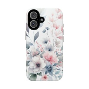 Può includere: Una custodia bianca per telefono con un design floreale ad acquerello. Il design include fiori rosa, blu e bianchi con foglie verdi e grigie. La custodia ha una finitura lucida e un modulo fotocamera nero.