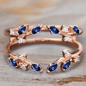 May include: A rose gold ring with a split design featuring marquise-shaped blue sapphires and round diamonds.