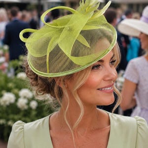 May include: A lime green fascinator hat featuring a circular base covered in fine mesh netting, accented with structured loops and upright feather details. The headpiece is constructed with a solid rim and a lightweight, semi-sheer fabric finish.