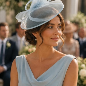 Può includere: Un cappello fascinator azzurro con un'ampia tesa circolare in rete e un complesso dettaglio a fiocco a strati sulla parte superiore. Il copricapo è realizzato in un tessuto rigido e semitrasparente che crea una silhouette strutturata.