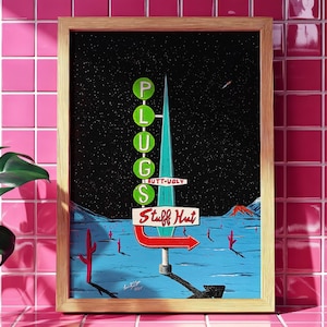 May include: A framed art print featuring a retro-style sign for "PLUGS" and "Stuff Hut" against a starry night sky. The sign is teal, red, and white, with a desert landscape and cacti in the foreground. The artwork is in a wooden frame.