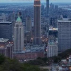 Könnte beinhalten: Eine Luftaufnahme einer Skyline mit hohen Gebäuden, darunter ein Wolkenkratzer mit einer spitzen Spitze. Die Gebäude sind größtenteils grau und weiß, und der Himmel ist hellblau.