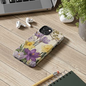 Könnte beinhalten: Eine Handyhülle mit einem Blumendesign mit lila und gelben Blumen auf cremefarbenem Hintergrund.