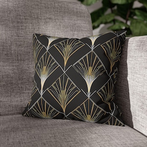 Könnte beinhalten: Schwarzes und goldenes Dekokissen mit einem geometrischen Muster aus überlappenden Diamantenformen und stilisierten Fächerdesigns.