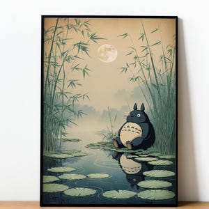 May include: Framed art print depicting a large, round, dark blue creature with a cream belly, seated beside a pond with lily pads. The background shows bamboo, a full moon, and a misty landscape, creating a tranquil atmosphere.