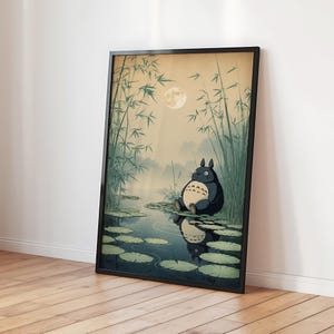 May include: Framed art print depicting a cartoon character in a pond scene. The artwork shows a full moon, bamboo, and a misty background. The character is dark blue with a cream belly, sitting on lily pads. The print is in a black frame.