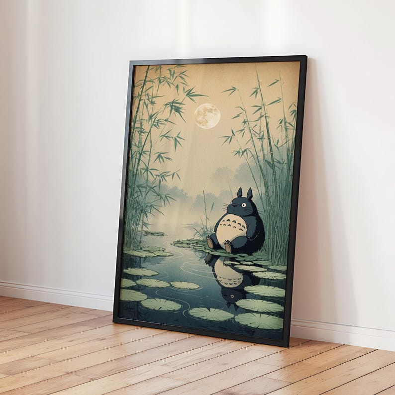 May include: Framed art print depicting a cartoon character in a pond scene. The artwork shows a full moon, bamboo, and a misty background. The character is dark blue with a cream belly, sitting on lily pads. The print is in a black frame.