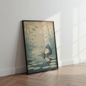 May include: Framed art print depicting a tranquil scene with a large, grey cartoon character seated on lily pads in a pond. The background features bamboo, a full moon, and a misty atmosphere. The artwork is presented in a black frame.