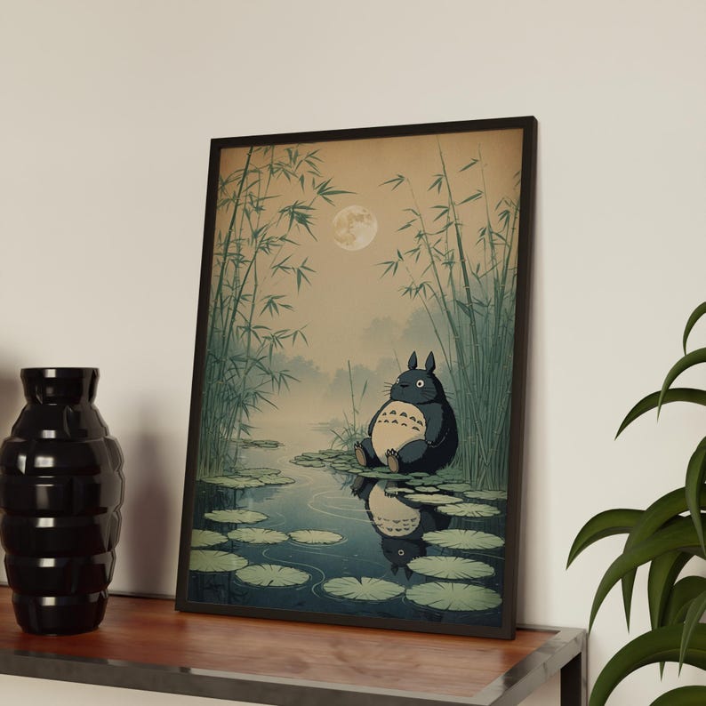 May include: Framed art print depicting a tranquil scene with a large, dark blue creature, similar to Totoro, sitting by a pond with lily pads. The artwork includes bamboo, a full moon, and a reflection in the water.