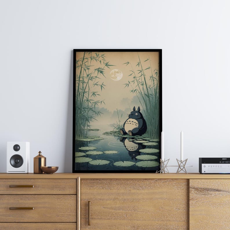 May include: Framed art print depicting a tranquil scene with a large, dark grey creature, similar to Totoro, seated on lily pads in a pond. The background features bamboo, a full moon, and a misty atmosphere, creating a peaceful, nature-themed artwork.