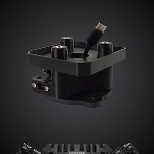 May include: A black racing wheel adapter featuring a central mounting plate with four cylindrical pillars and a protruding USB-C cable. Below, a carbon fibre textured steering wheel rim displays the text FANATEC and THRUSTMASTER with various buttons.
