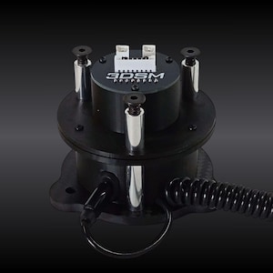 May include: A black cylindrical electronic component featuring the text 3DSM printed on the top surface. It includes a white electrical connector, three vertical silver metal support pillars with black screws, and a black coiled cable extending outward.