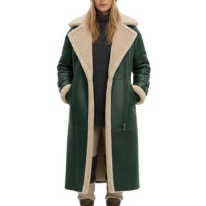 May include: A long, forest green coat with a cream-colored shearling lining and trim. The coat features a wide lapel, a zipper closure, and pockets. The sleeves have a buckle detail at the cuffs. The coat is knee-length and appears to be made of leather.