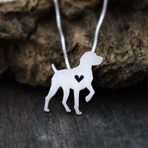 May include: A silver necklace featuring a cutout silhouette of a German Shorthaired Pointer dog with a heart in the centre. The necklace is displayed on a wooden surface.