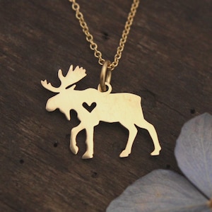 May include: A gold-toned necklace featuring a moose-shaped pendant with a small heart-shaped cutout in the center of the body. The pendant is suspended from a delicate gold-toned chain, showcasing a smooth, metallic finish and a clean silhouette.