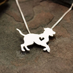 May include: A silver necklace with a cutout silhouette of a dog with a heart in its chest. The necklace is on a dark gray background.
