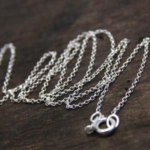 May include: A silver chain necklace with a lobster clasp closure. The chain is made of small, round links.