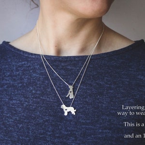 May include: Two silver necklaces layered on a person wearing a blue shirt. The top necklace has a small dog pendant with a heart cutout. The bottom necklace has a larger dog pendant with a heart cutout. The text "Layering is an excellent way to wear two pendants! This is a 16" Box chain and an 18" Rolo chain" is visible in the image.
