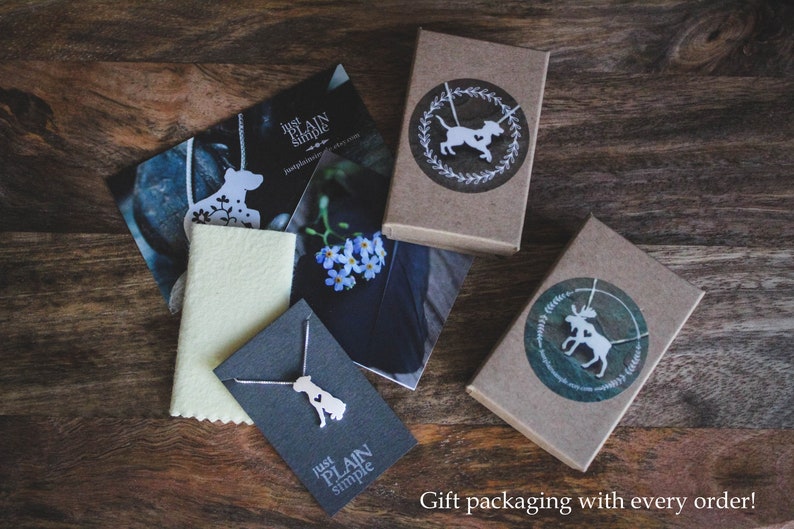 May include: Three gift boxes with brown paper wrapping and white silhouette designs of a dog, a moose, and a dog on a necklace. The boxes are on a wooden surface. The text "Just Plain Simple" is on two of the boxes.