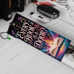 May include: A colorful bookmark with the text "Every Book is a Door" and illustrations of keys and an open book. The bookmark is inserted into a book, with a black cord and charm attached.