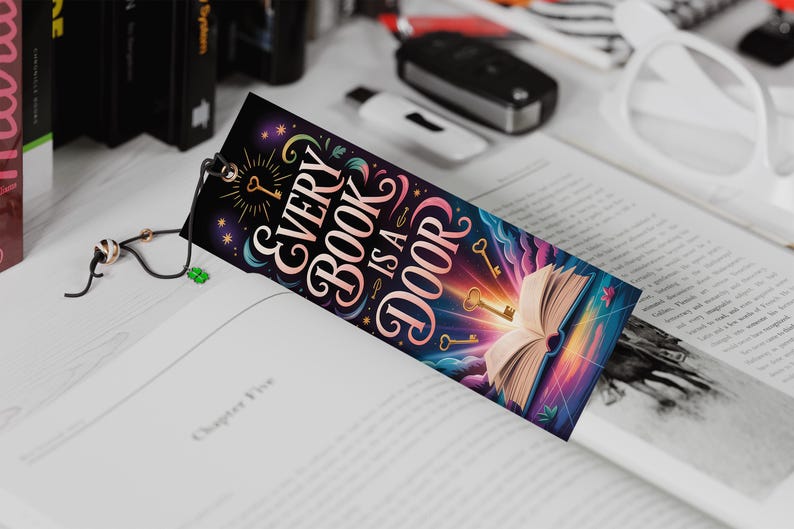 May include: A colorful bookmark with the text "Every Book is a Door" and illustrations of keys and an open book. The bookmark is inserted into a book, with a black cord and charm attached.