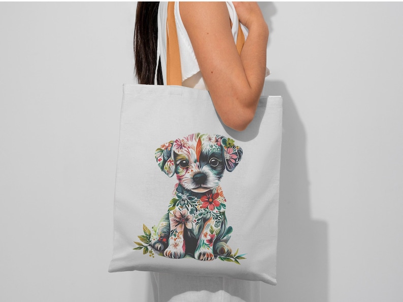 May include: White tote bag featuring a colorful illustration of a puppy adorned with floral patterns. The puppy has a black and white face and is surrounded by flowers in shades of pink, red, and green. The bag is held by a person.