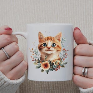 May include: White ceramic mug featuring a watercolor illustration of a ginger tabby cat with blue eyes, surrounded by floral elements. The cat's portrait is centered on the mug, creating a charming and artistic design.