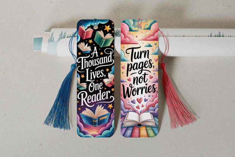 May include: Two colorful bookmarks with tassels. One features the text "A Thousand Lives, One Reader" with illustrations of books and stars. The other says "Turn pages, not worries" with hearts and book illustrations. Both have a tassel.