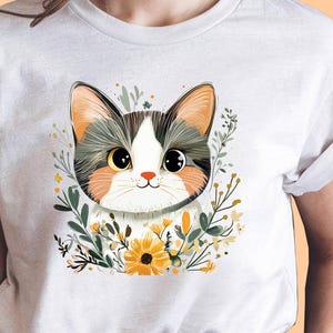May include: A light gray t-shirt featuring a cute cat illustration. The cat has big eyes, a white face, and is surrounded by flowers and greenery. The cat's ears are orange and gray. The shirt is made of a soft material.