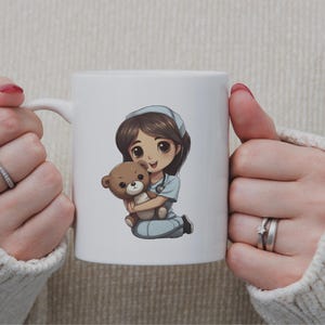 May include: White ceramic mug featuring a cartoon illustration of a nurse holding a teddy bear. The nurse is wearing a blue uniform and a white cap.