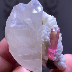 May include: A pink and green tourmaline crystal with a clear quartz crystal on a white matrix.