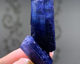 Könnte beinhalten: Nahaufnahme einer tiefblauen Kristallformation. Der Kristall hat eine säulenartige Struktur mit sichtbaren Streifen und einer rauen, strukturierten Oberfläche. Die Farbe ist ein sattes, sattes Blau mit Farbvariationen. Der Kristall wird von einer Person gehalten.